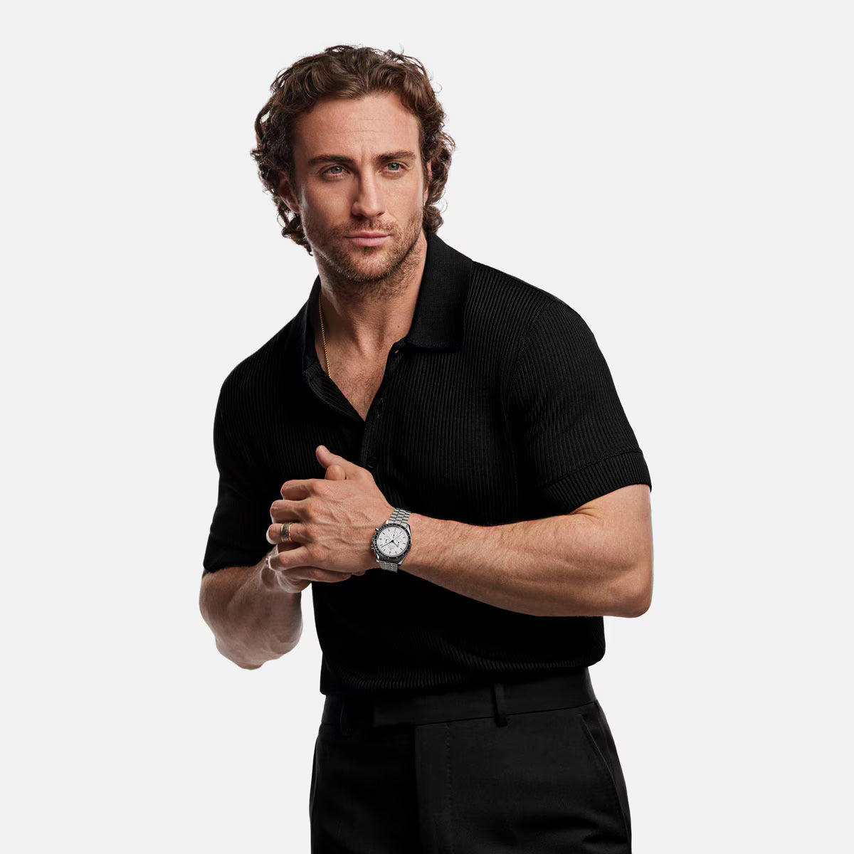 Man wearing a black polo shirt and black pants with an Omega white dial moonwatch on a white background